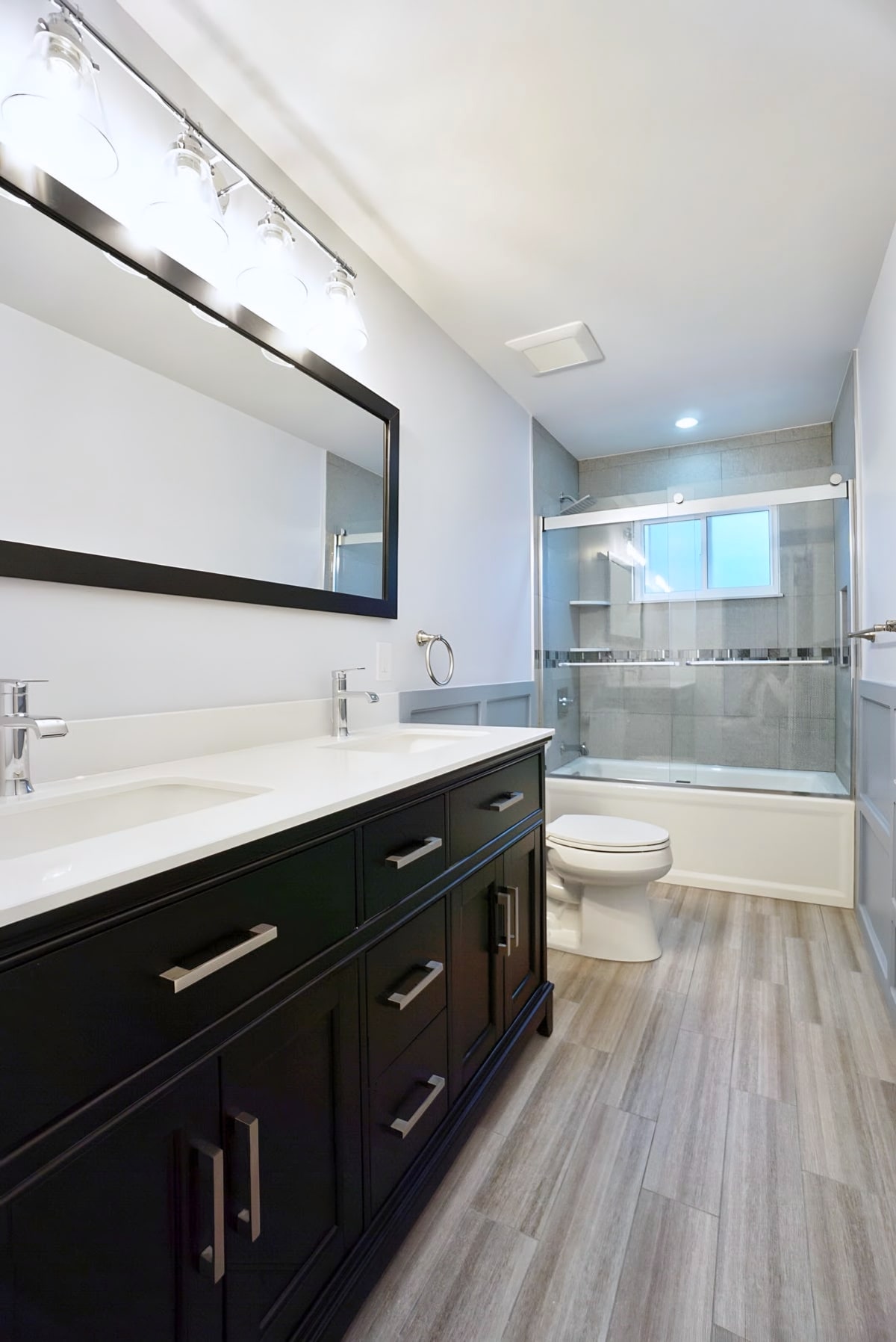 Remodeled bathroom with dark double vanity and glass-door tub shower